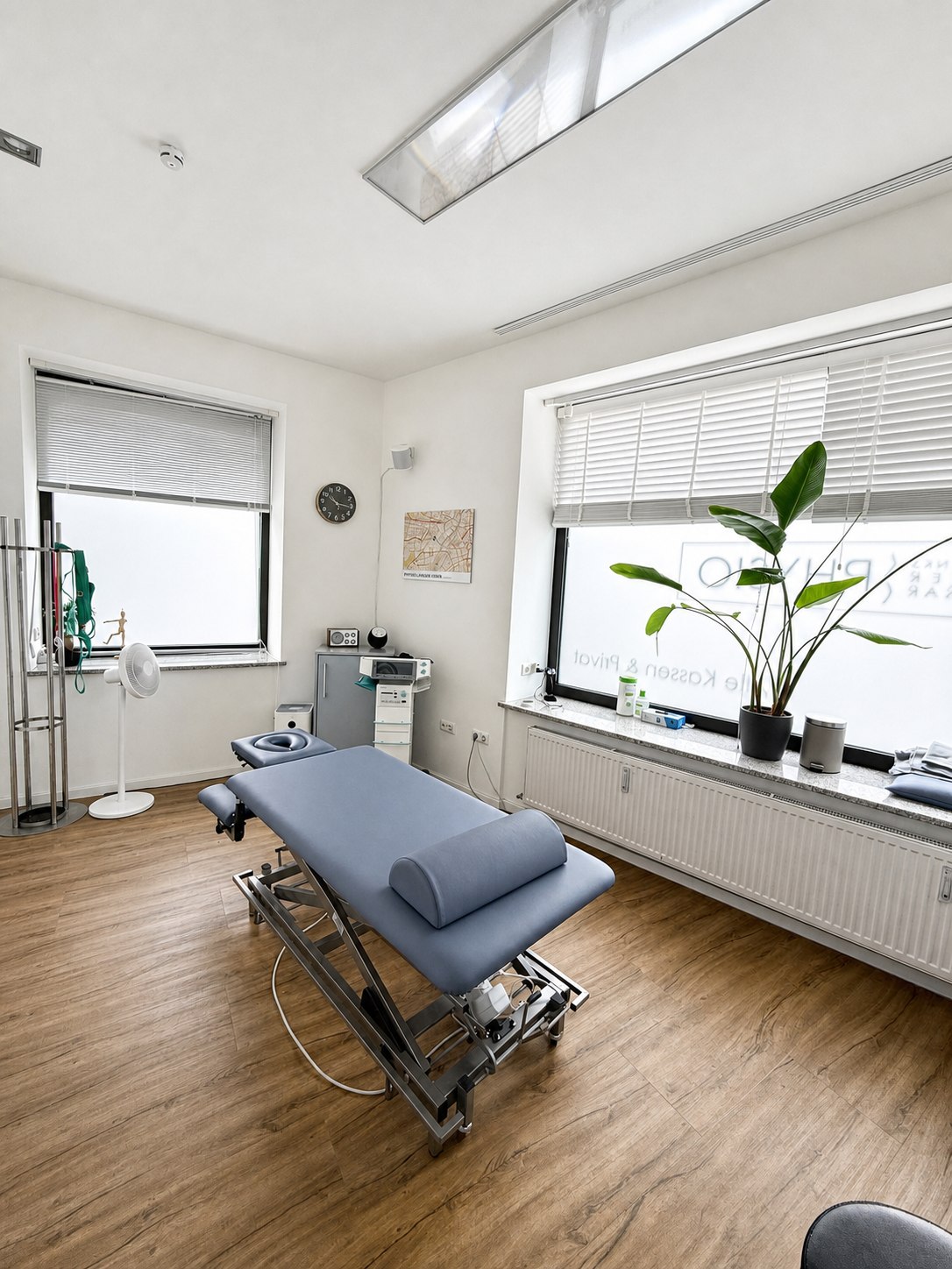 Heller Behandlungsraum mit zwei Fenstern und Therapieliege