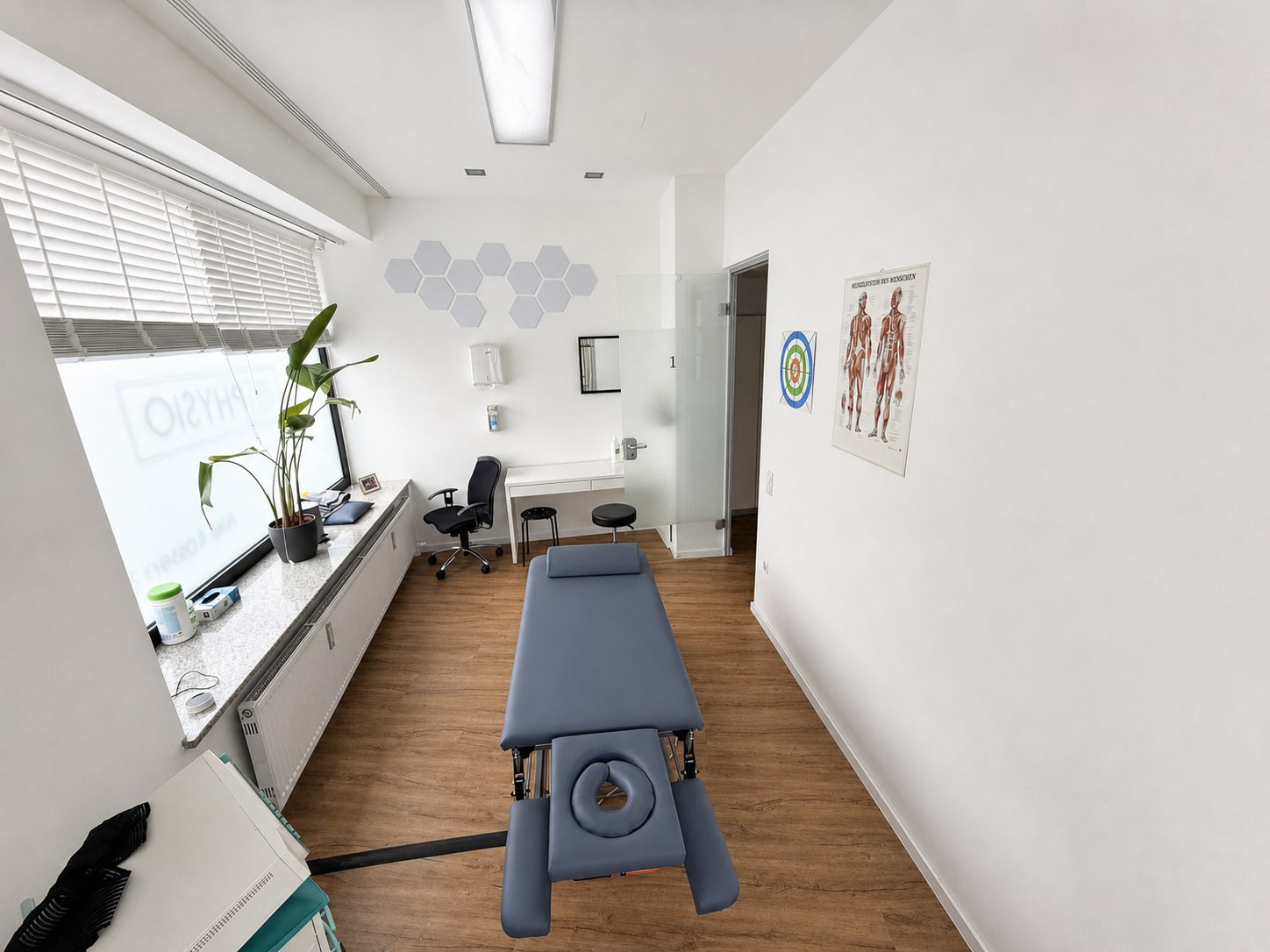 Behandlungsraum mit Therapieliege und Blick zum Schreibtisch